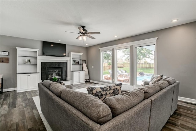 living room with a fireplace, ceiling fan, dark wood-type flooring, and built in features