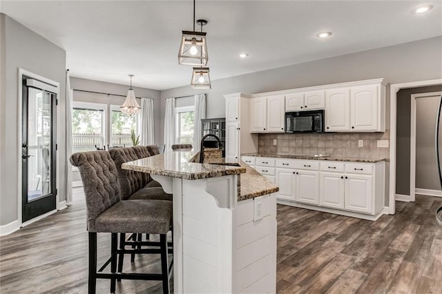 kitchen with decorative light fixtures, white cabinetry, tasteful backsplash, sink, and dark stone counters