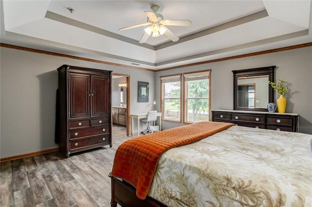 bedroom with light hardwood / wood-style floors, ensuite bath, ceiling fan, and a tray ceiling