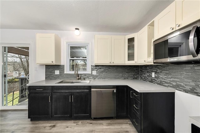 kitchen featuring appliances with stainless steel finishes, tasteful backsplash, sink, white cabinets, and light hardwood / wood-style floors