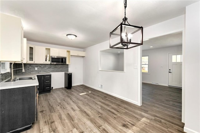 kitchen with sink, white cabinetry, wood-type flooring, decorative light fixtures, and backsplash