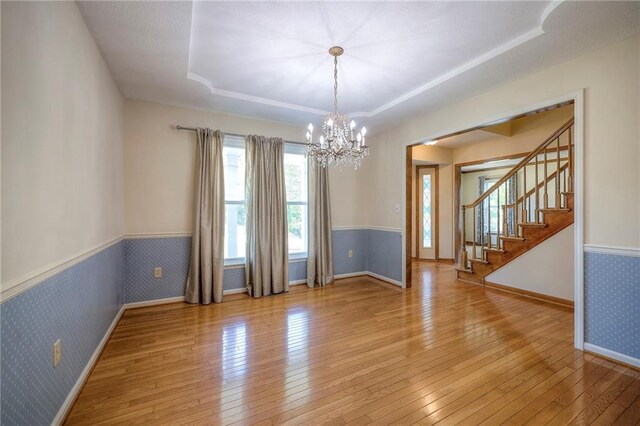 spare room with light wood-type flooring, a raised ceiling, and a notable chandelier