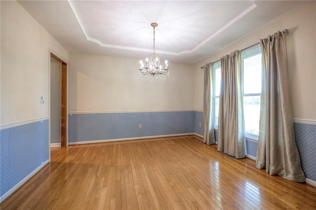 empty room with light hardwood / wood-style flooring, an inviting chandelier, and a tray ceiling