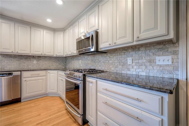 kitchen with white cabinets, appliances with stainless steel finishes, light hardwood / wood-style floors, and dark stone counters