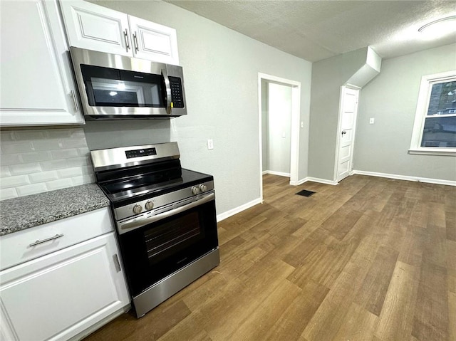 kitchen with decorative backsplash, light hardwood / wood-style flooring, white cabinets, appliances with stainless steel finishes, and dark stone countertops