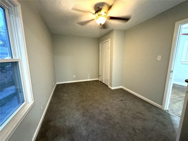 unfurnished bedroom featuring ceiling fan, a textured ceiling, dark carpet, and multiple windows