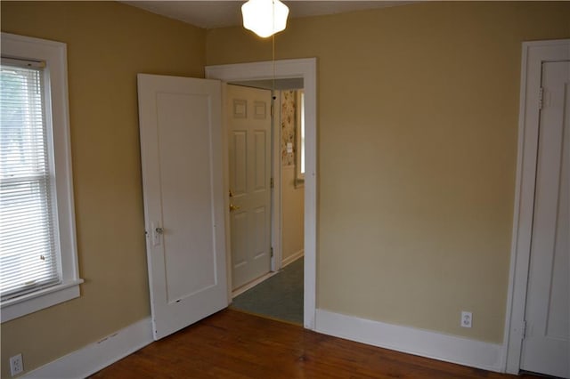 unfurnished bedroom featuring multiple windows, baseboards, and wood finished floors