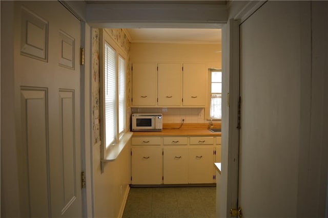 kitchen with white cabinets, white microwave, light countertops, crown molding, and light floors