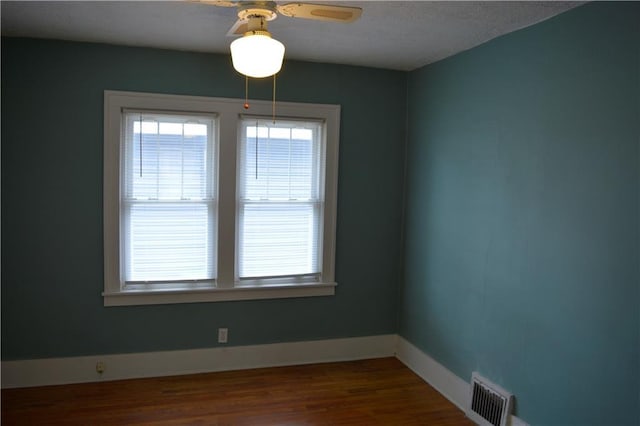 empty room with a ceiling fan, wood finished floors, visible vents, and baseboards