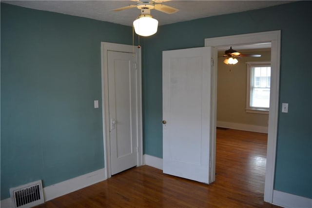 empty room with a ceiling fan, wood finished floors, visible vents, and baseboards