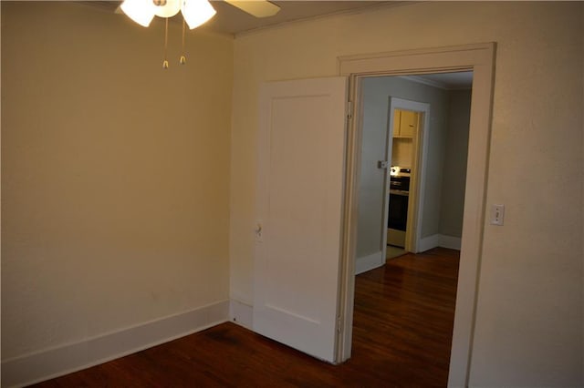 spare room with dark wood-type flooring, crown molding, baseboards, and a ceiling fan