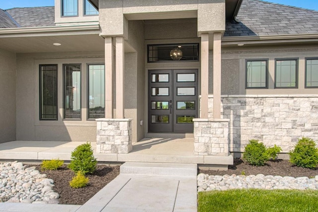 entrance to property with stone siding, roof with shingles, french doors, and stucco siding