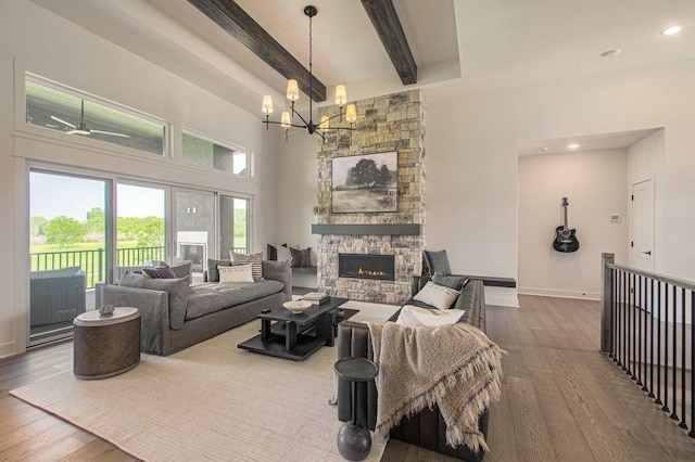 living area with a stone fireplace, hardwood / wood-style flooring, a towering ceiling, baseboards, and beamed ceiling