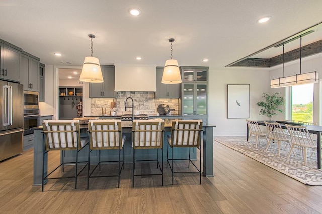 kitchen featuring wood finished floors, a kitchen breakfast bar, appliances with stainless steel finishes, decorative backsplash, and a center island with sink