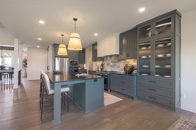 kitchen featuring stainless steel appliances, dark countertops, custom range hood, decorative backsplash, and dark wood-type flooring