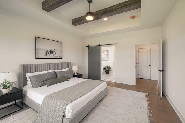 bedroom featuring a barn door, baseboards, wood finished floors, and beamed ceiling