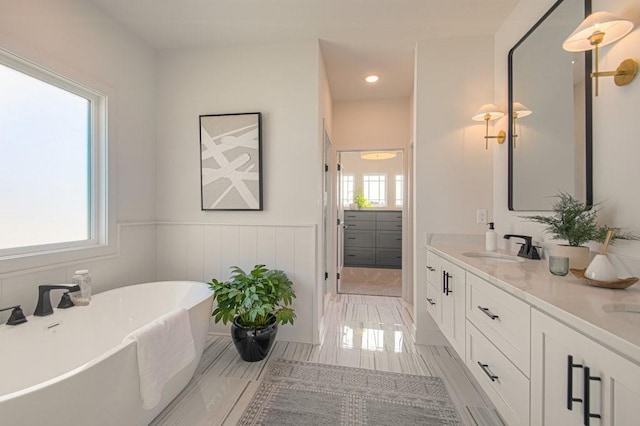 bathroom with a wainscoted wall, double vanity, a freestanding bath, and a sink