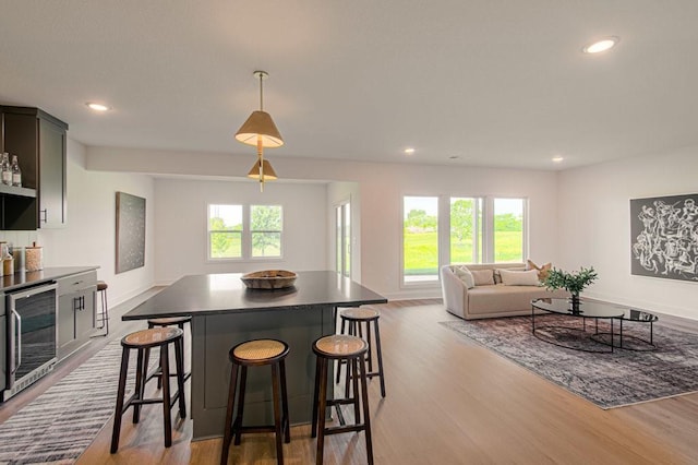 kitchen with a kitchen bar, wine cooler, wood finished floors, and a center island