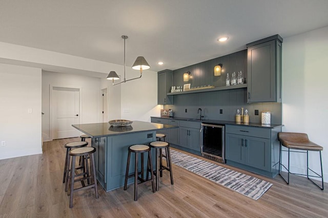 kitchen featuring dark countertops, light wood-type flooring, wine cooler, and a breakfast bar area