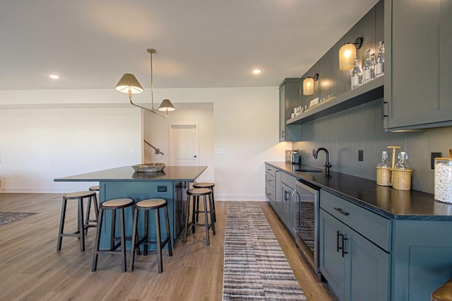 kitchen with a breakfast bar, dark countertops, a sink, a kitchen island, and beverage cooler