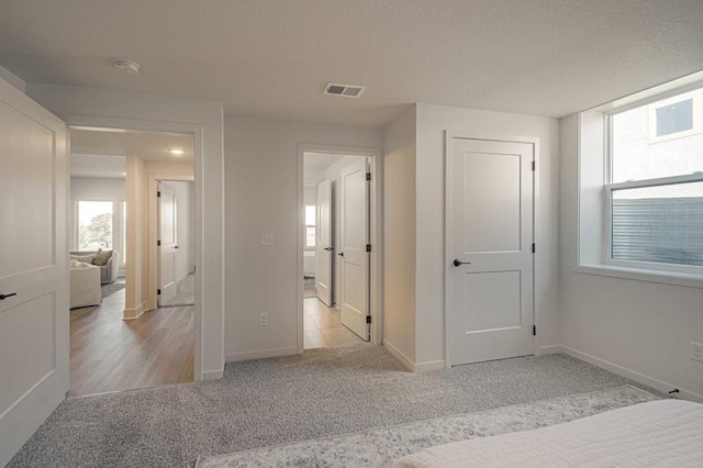 unfurnished bedroom with a textured ceiling, carpet, visible vents, and baseboards