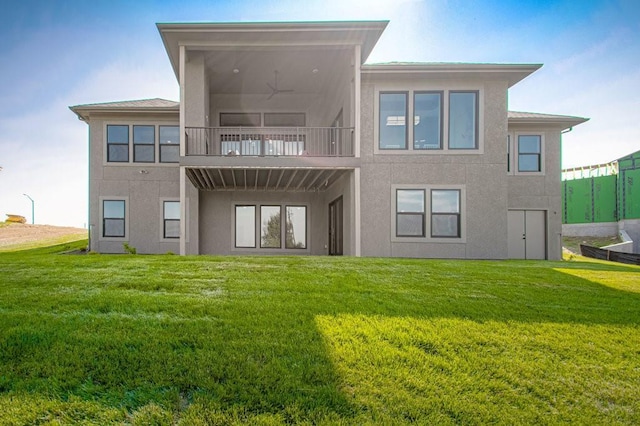 back of house featuring a lawn, a balcony, and stucco siding