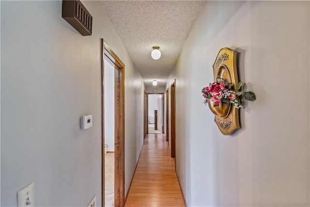 corridor with a textured ceiling and light hardwood / wood-style floors