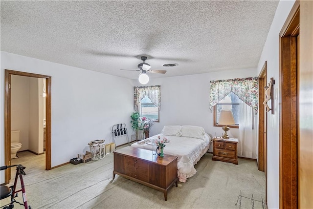 bedroom with ceiling fan, light colored carpet, ensuite bathroom, and a textured ceiling