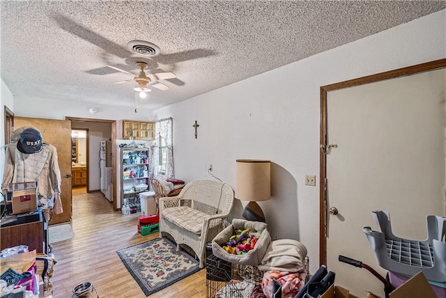 living room with ceiling fan, light hardwood / wood-style floors, and a textured ceiling