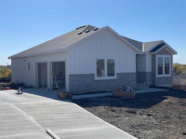 rear view of house featuring a patio area, roof with shingles, board and batten siding, and stone siding