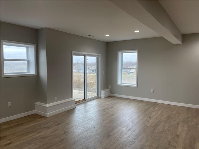 spare room featuring a wealth of natural light, beam ceiling, and light wood-type flooring