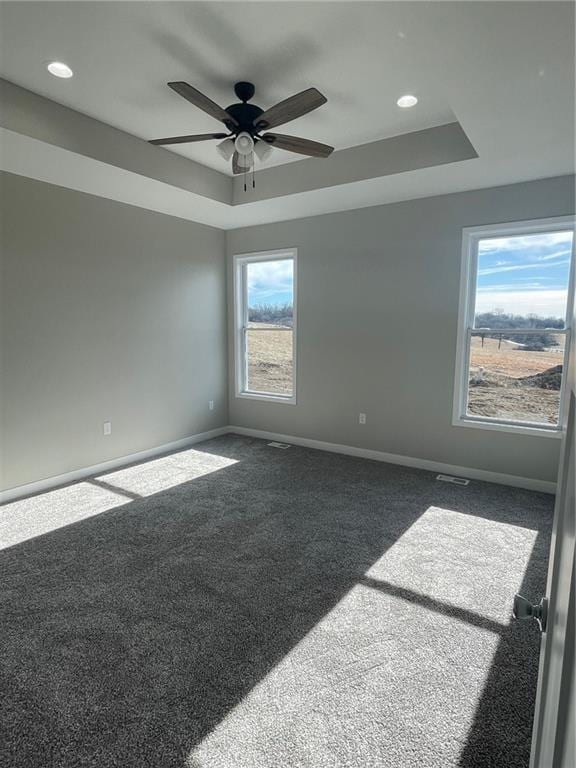 empty room featuring dark carpet, a raised ceiling, and ceiling fan