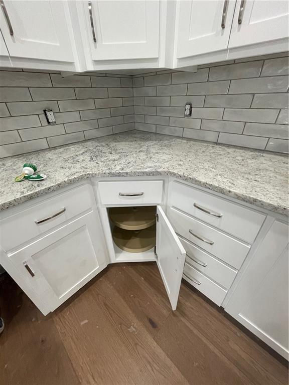 room details with decorative backsplash, light stone countertops, dark hardwood / wood-style floors, and white cabinets