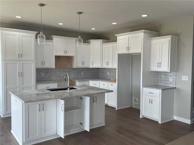 kitchen with pendant lighting, white cabinetry, sink, light stone counters, and a center island with sink