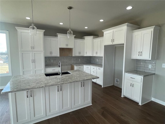 kitchen featuring sink, white cabinetry, hanging light fixtures, an island with sink, and light stone countertops