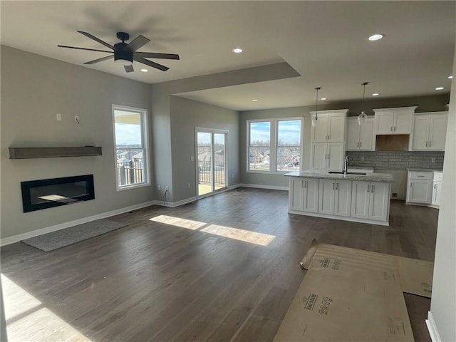 kitchen with white cabinetry, dark hardwood / wood-style floors, a center island with sink, and pendant lighting