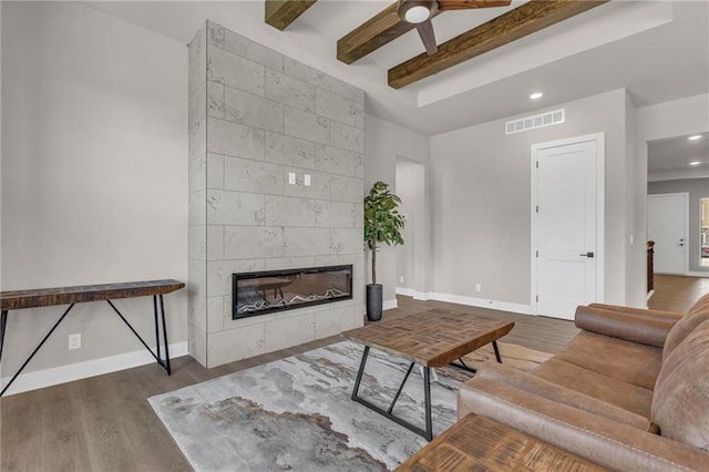 living room featuring ceiling fan, dark hardwood / wood-style floors, beam ceiling, and a fireplace