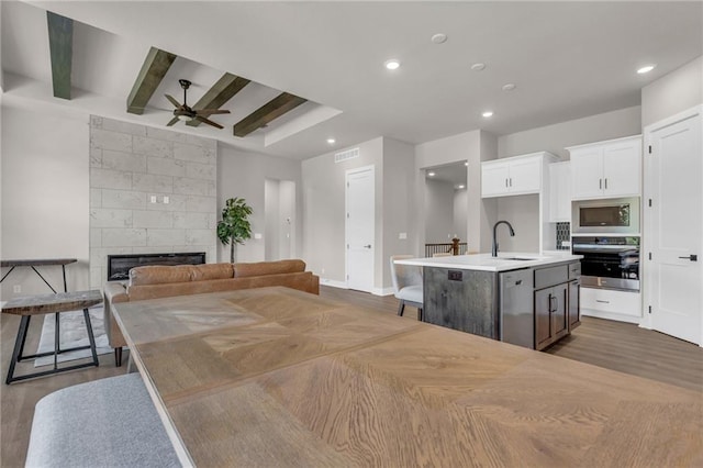 kitchen featuring a fireplace, appliances with stainless steel finishes, beamed ceiling, an island with sink, and ceiling fan