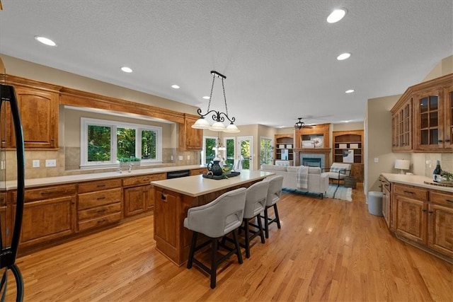 kitchen featuring decorative light fixtures, light hardwood / wood-style flooring, a fireplace, a kitchen island, and a breakfast bar area