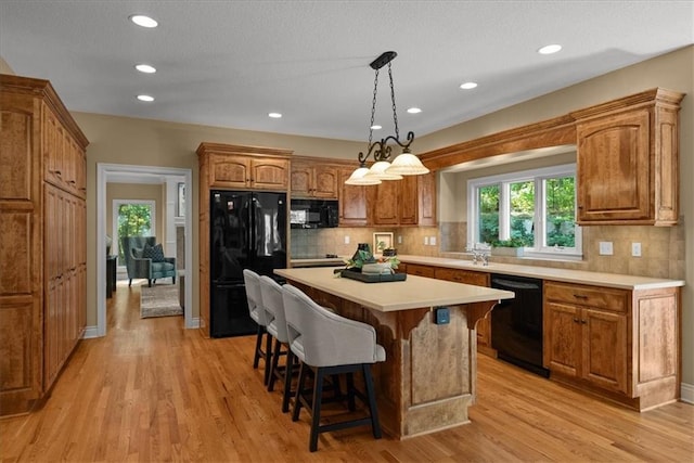 kitchen featuring tasteful backsplash, black appliances, light hardwood / wood-style floors, a kitchen island, and a breakfast bar area