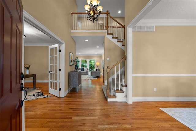 foyer entrance with hardwood / wood-style floors, crown molding, and a notable chandelier