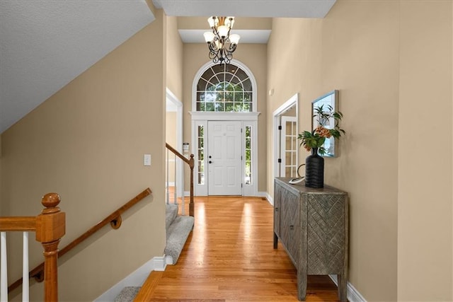 foyer with light hardwood / wood-style floors, a towering ceiling, and an inviting chandelier