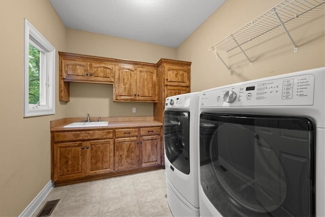 washroom with a textured ceiling, cabinets, sink, and washing machine and clothes dryer