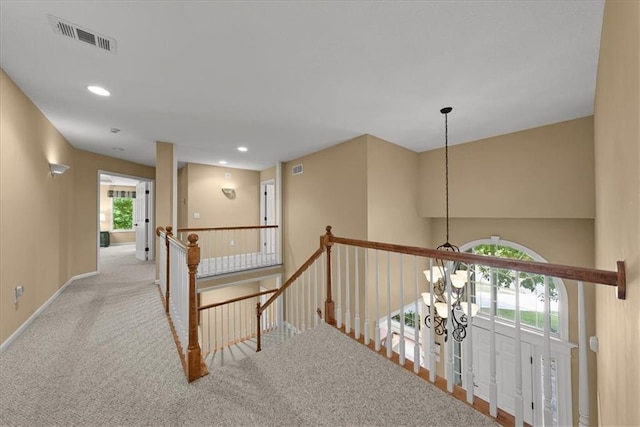 corridor with light colored carpet and an inviting chandelier