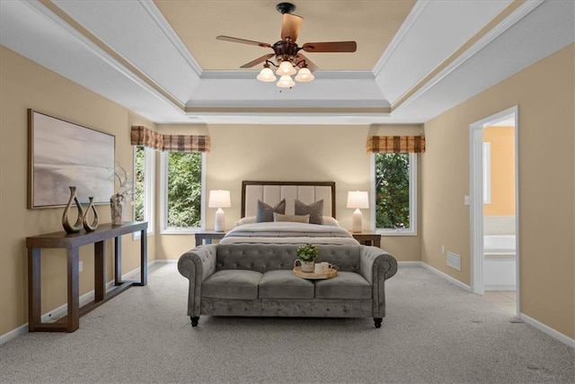 carpeted bedroom with a tray ceiling, ceiling fan, ensuite bathroom, and ornamental molding