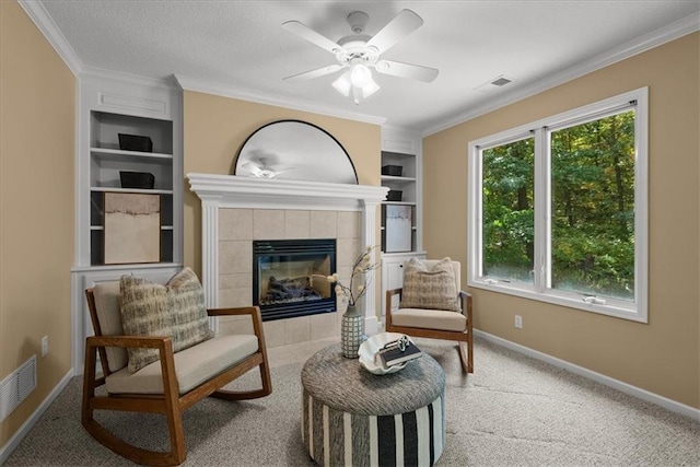 sitting room featuring carpet flooring, built in shelves, crown molding, and a tile fireplace