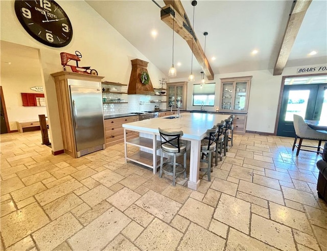 kitchen with hanging light fixtures, tasteful backsplash, a breakfast bar area, built in fridge, and beam ceiling