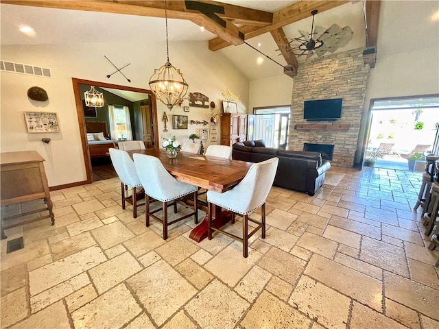 dining room with high vaulted ceiling, beam ceiling, ceiling fan with notable chandelier, and a stone fireplace