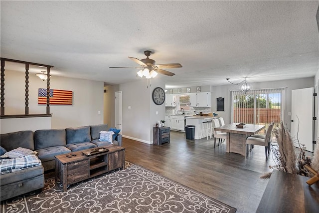 living room featuring ceiling fan with notable chandelier, dark hardwood / wood-style floors, sink, and a textured ceiling