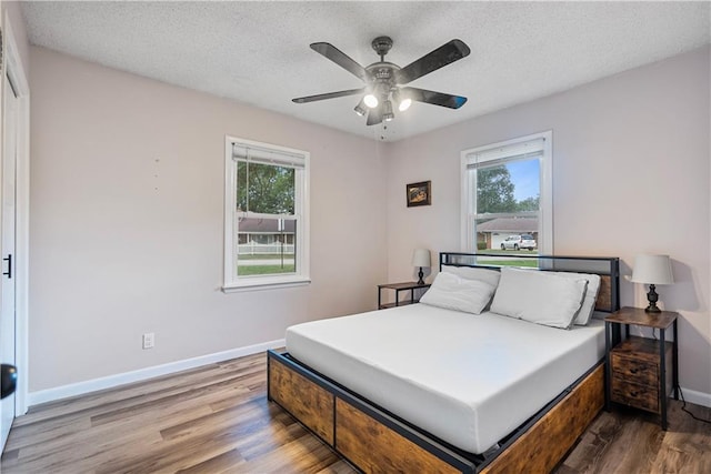 bedroom featuring multiple windows, dark hardwood / wood-style flooring, ceiling fan, and a textured ceiling